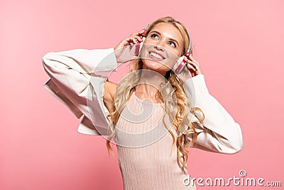 Dreamy blonde happy woman listening music in headphones isolated on pink Stock Photo