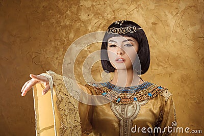 Beautiful Egyptian woman like Cleopatra pointing finger away on golden background Stock Photo