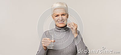 Beautiful elderly woman taking vitamin supplements over light studio background Stock Photo