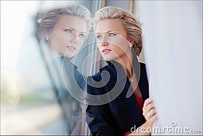 Beautiful elegant exquisite blonde girl looks through the glass, reflecting in it Stock Photo