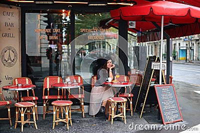 Beautiful elegant girl in Paris sits in a Parisian cafe and drinks coffee with a croissant Editorial Stock Photo