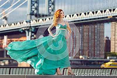 Beautiful elegant red haired woman standing near Manhattan Bridge in New York City wearing long green dress. Stock Photo