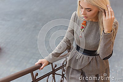Beautiful elegant slim blonde girl in elegant dress with brooch up the stairs in the city Stock Photo