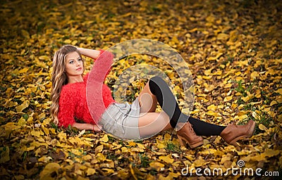 Beautiful elegant woman with red blouse and short skirt posing in park during fall. Young pretty woman with blonde hair lying down Stock Photo