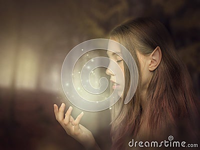 Beautiful elf girl portrait close-up in the forest looking at the glow on her hand. Fantasy photo art Stock Photo