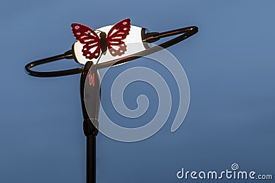 A fabric butterfly rests on a lighted lamp against the blue sky at dusk Stock Photo