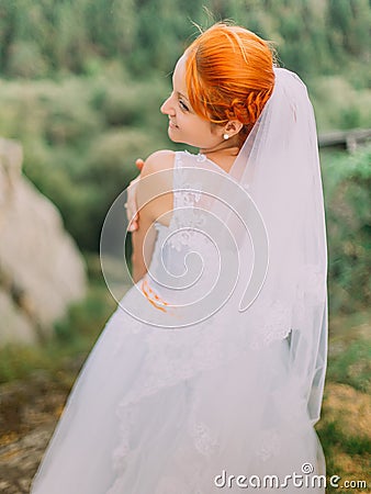 Beautiful fabulous happy redhair bride looking over shoulder on background of Carpathians mountains Stock Photo
