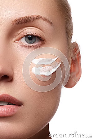 Beautiful face of young woman with cosmetic cream on a cheek. Skin care concept. Closeup portrait isolated on white. Close-up Stock Photo