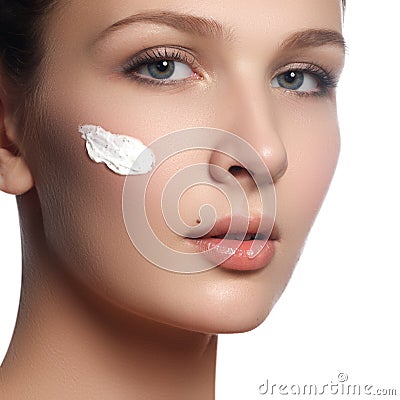 Beautiful face of young woman with cosmetic cream on a cheek. Skin care concept. Closeup portrait isolated on white. Close-up Stock Photo