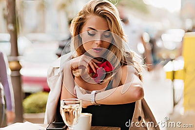 Beautiful fair-haired woman looking at wristwatch while drinking coffee at outdoor restaurant. Portrait of serious lady Stock Photo