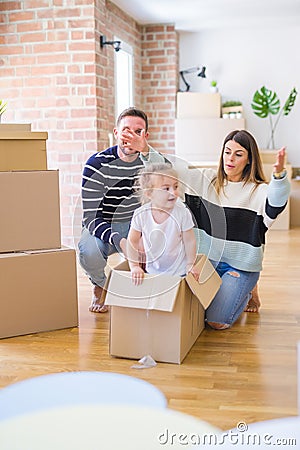 Beautiful famiily, kid playing with his parents riding cardboard fanny box at new home Stock Photo