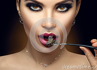 Beautiful Fashion Model woman eating black caviar. Beauty girl portrait with caviar on her lips. Female with spoon of black Caviar Stock Photo