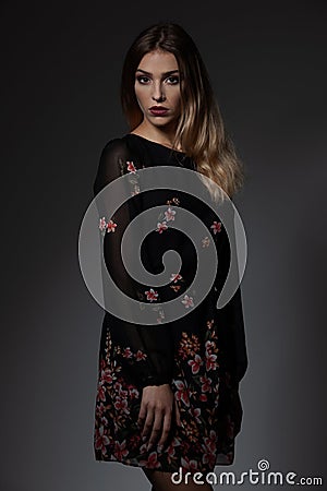 Beautiful fashionable woman in black dress with floral patern over dark gray background Stock Photo