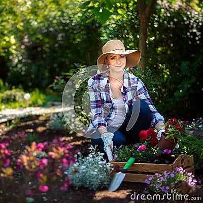 Beautiful female gardener looking at camera smiling and holding wooden crate full of flowers ready to be planted in her garden. Stock Photo