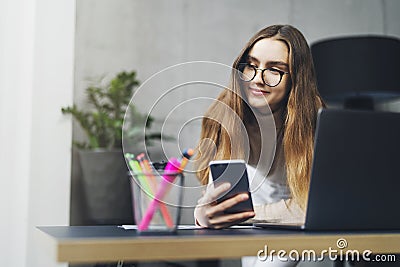 Beautiful female in glasse doing creative project on laptop. Woman sitting by computer at office desk. Digital tools and solutions Stock Photo