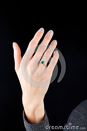 Beautiful female hand with gold ring with diamonds and emerald on black background Stock Photo