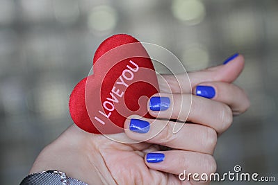 Beautiful female hand with manicure holds a plush heart. Bright blue nail polish. Stock Photo