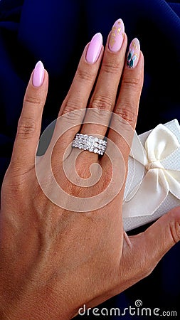 Beautiful female hand with ring with diamonds on a dark blue fabric background with a gift box Stock Photo
