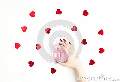 Beautiful female hand with trendy red manicure holding stylish bottle of perfume with spray of vibrant red heart-shaped Stock Photo