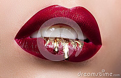 Beautiful female lips closeup. Red lipstick, gold paint flowing over his lips. Stock Photo Stock Photo