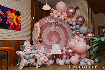 Beautiful festive decorations, pink and grey balloons arch, wooden stars, white chair and number one balloon on wooden round Editorial Stock Photo