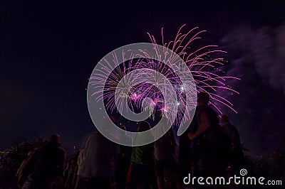 Beautiful firework scene with people as silhouttes watching at the colorful violett rockets at the night sky. Stock Photo