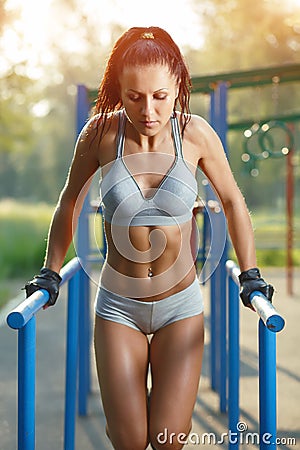 Beautiful fitness woman doing exercise on parallel bars sunny outdoor Stock Photo