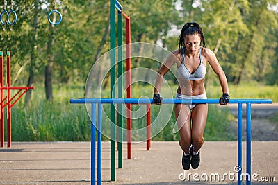 Beautiful fitness woman doing exercise on parallel bars sunny outdoor Stock Photo