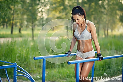 Beautiful fitness woman doing exercise on parallel bars sunny outdoor Stock Photo