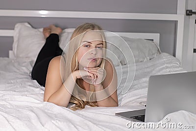 Beautiful flirty blonde with laptop on bed with white sheets. pretty people at isolation Stock Photo