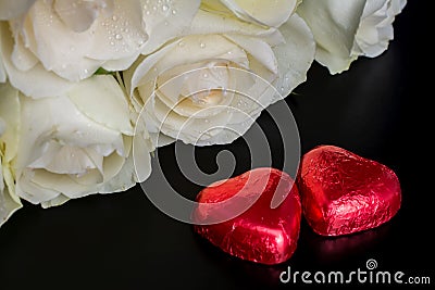 Beautiful flowers on black background with cream roses bouquet and chocolates red heart shaped Stock Photo