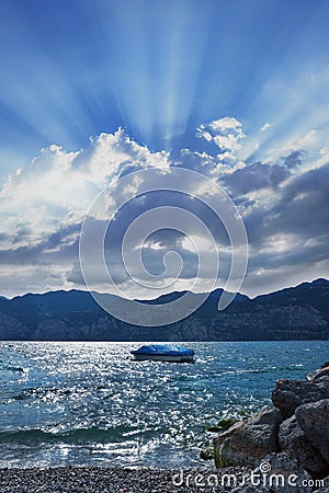 Lake garda with boat and dramatic cloud and sunbeams Stock Photo