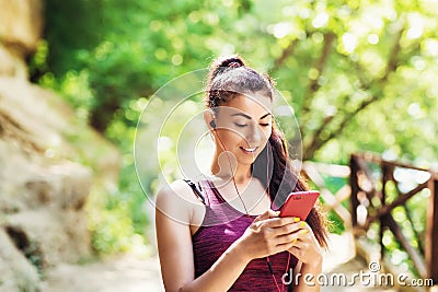 Beautiful girl athlete chooses a track in a smartphone. Portrait of a beautiful sports model in the park with a phone in his hand Stock Photo