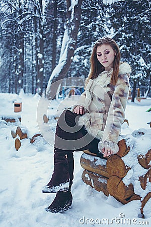 Beautiful girl in a beige short coat with flowing hair is sitting on a wooden frame Stock Photo