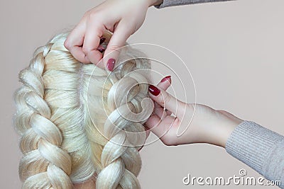 Beautiful girl with blonde hair, hairdresser weaves a braid close-up, in a beauty salon. Stock Photo