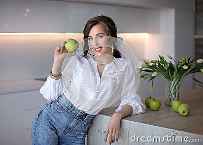 A beautiful girl in blue jeans and a white shirt holds a green Apple. Portrait of a young lady Stock Photo
