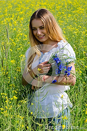 Beautiful girl with bouquet of cornflowers on flowering rapeseed Stock Photo