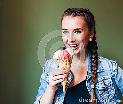 Beautiful girl with braids sitting in a cafe and eating huge multi-colored ice cream in a waffle cone. Smiling at the camera Stock Photo