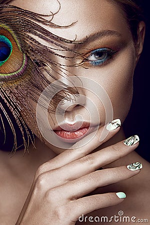 Beautiful girl with bright makeup, manicure design and peacock feather on her face. Art nails. Stock Photo