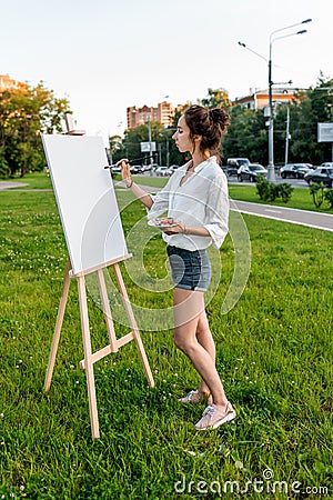 Beautiful girl city summer, woman artist, draws picture road, beginning of drawing, first brush stroke, white canvas Stock Photo
