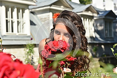 Beautiful girl with curls next to red roses in the garden Stock Photo
