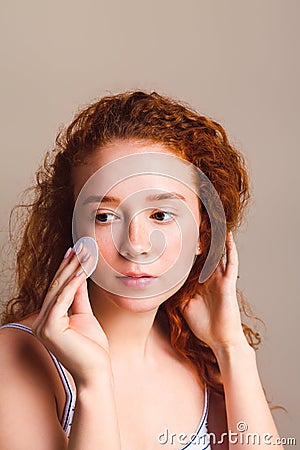 Beautiful girl with curly hair in the studio on a beige background. In hand a cotton pad, wipes his face. No makeup, close up Stock Photo