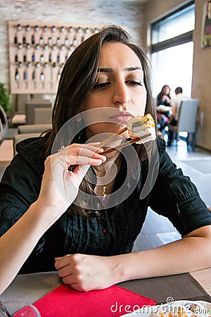 Beautiful girl with dark hair, dressed in black is holding chopsticks with sushi Stock Photo