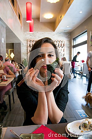 Beautiful girl with dark hair, dressed in black is holding chopsticks and temaki sushi Stock Photo