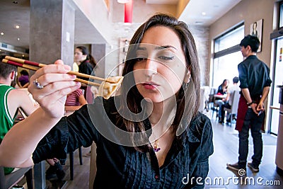 Beautiful girl with dark hair, dressed in black is holding meat ravioli with chopsticks Stock Photo