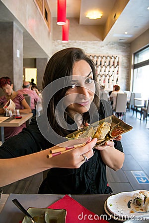 Beautiful girl with dark hair, dressed in black is holding a plate full of meat rolls and chilly sauce Stock Photo