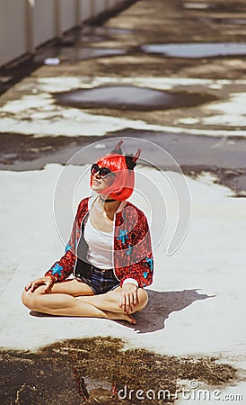 Beautiful girl devil sitting on city background near the puddle with his reflection. In anticipation of Halloween Stock Photo