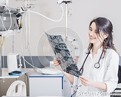 Beautiful girl doctor in a white coat examines X-ray photo of the patient to identify the problem. Professional conversation, cons Stock Photo