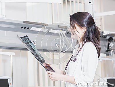 Beautiful girl doctor in a white coat examines X-ray photo of the patient to identify the problem. Professional conversation, cons Stock Photo