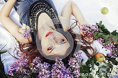 Beautiful girl in dress posing lying in lilac branches on a summer day, purple flowers in the Park. Spring portrait of a dreaming Stock Photo